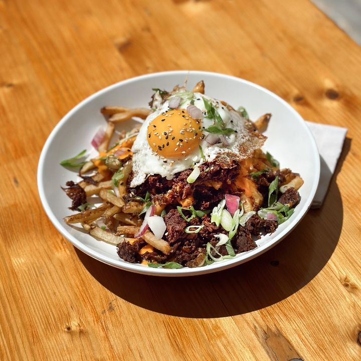 Hands sharing a plate of kimchi fries on the patio at HOMES Brewery Brewpub